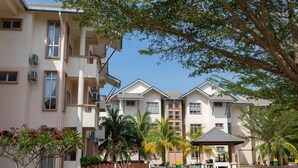 A multi-story residential building with balconies, a small garden area with palm trees, and a covered seating area. - Seri Bayu Resort (Sungai Pelek)