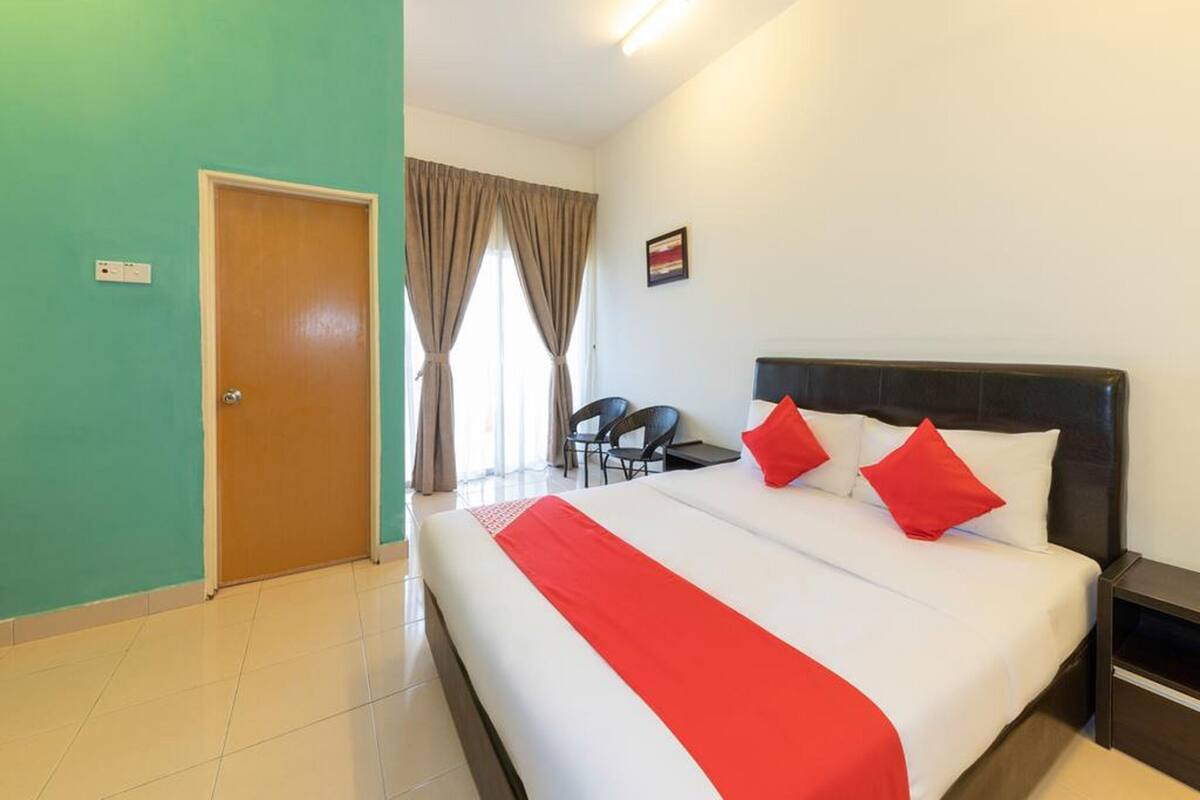 Une chambre d’hôtel comprenant un lit, une table de chevet, une chaise, un bureau, une fenêtre avec des rideaux et une porte.