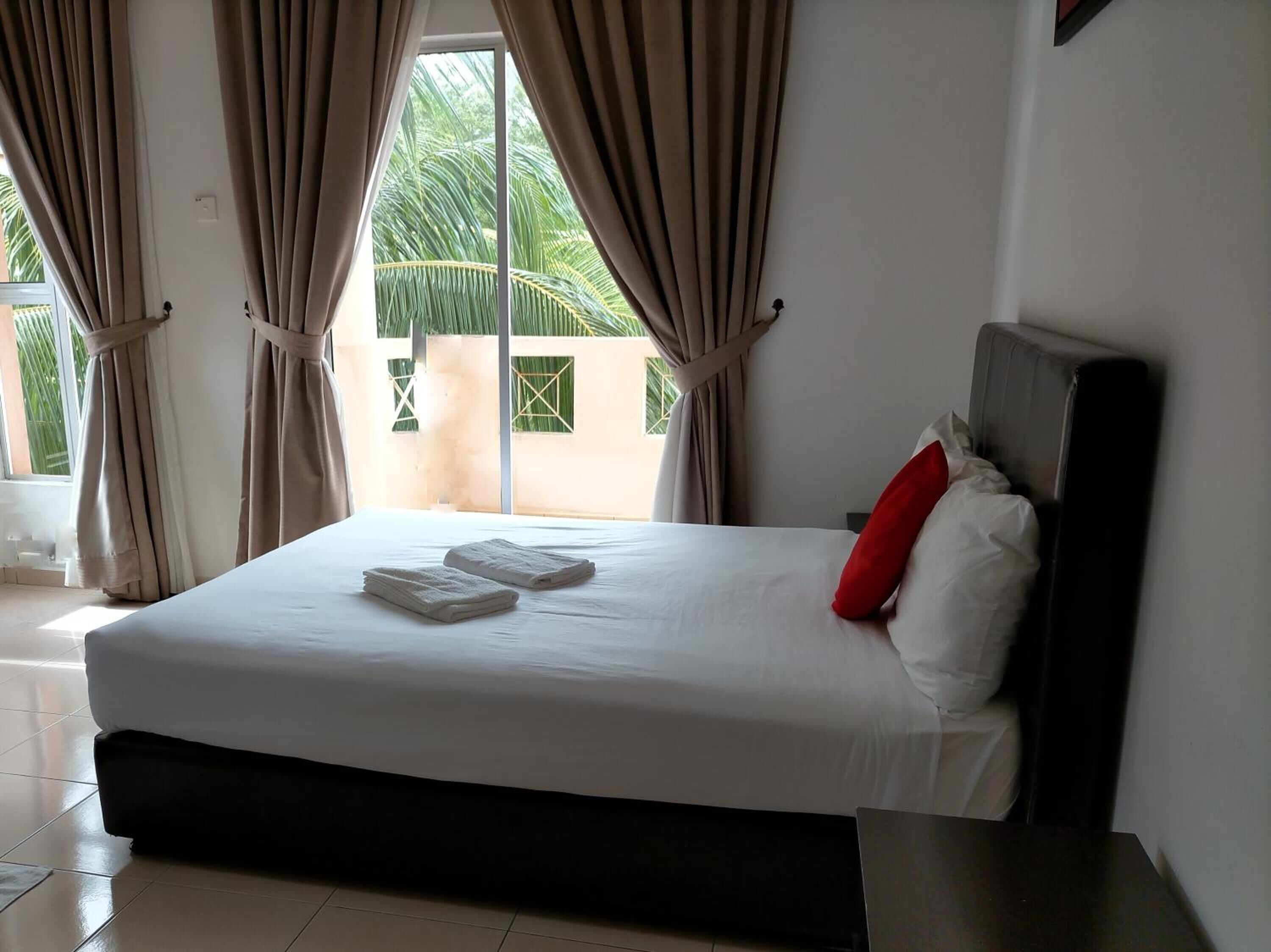 Una habitación de hotel con una cama grande, cortinas color beige y vistas a palmeras a través de la ventana.