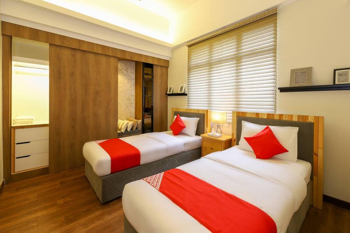 Une chambre d’hôtel avec deux lits, un plancher en bois, une armoire intégrée, un ventilateur de plafond et une fenêtre avec des stores.