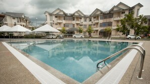 A swimming pool with a tiled deck, surrounded by buildings with balconies and a covered area with umbrellas. - Seri Bayu Resort (Sungai Pelek)