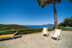 A stone patio with two white lounge chairs and a yellow bench overlooking a coastal landscape. - APP.TI CASA SERENA - CASA SERENA MONO 6 (Capoliveri)