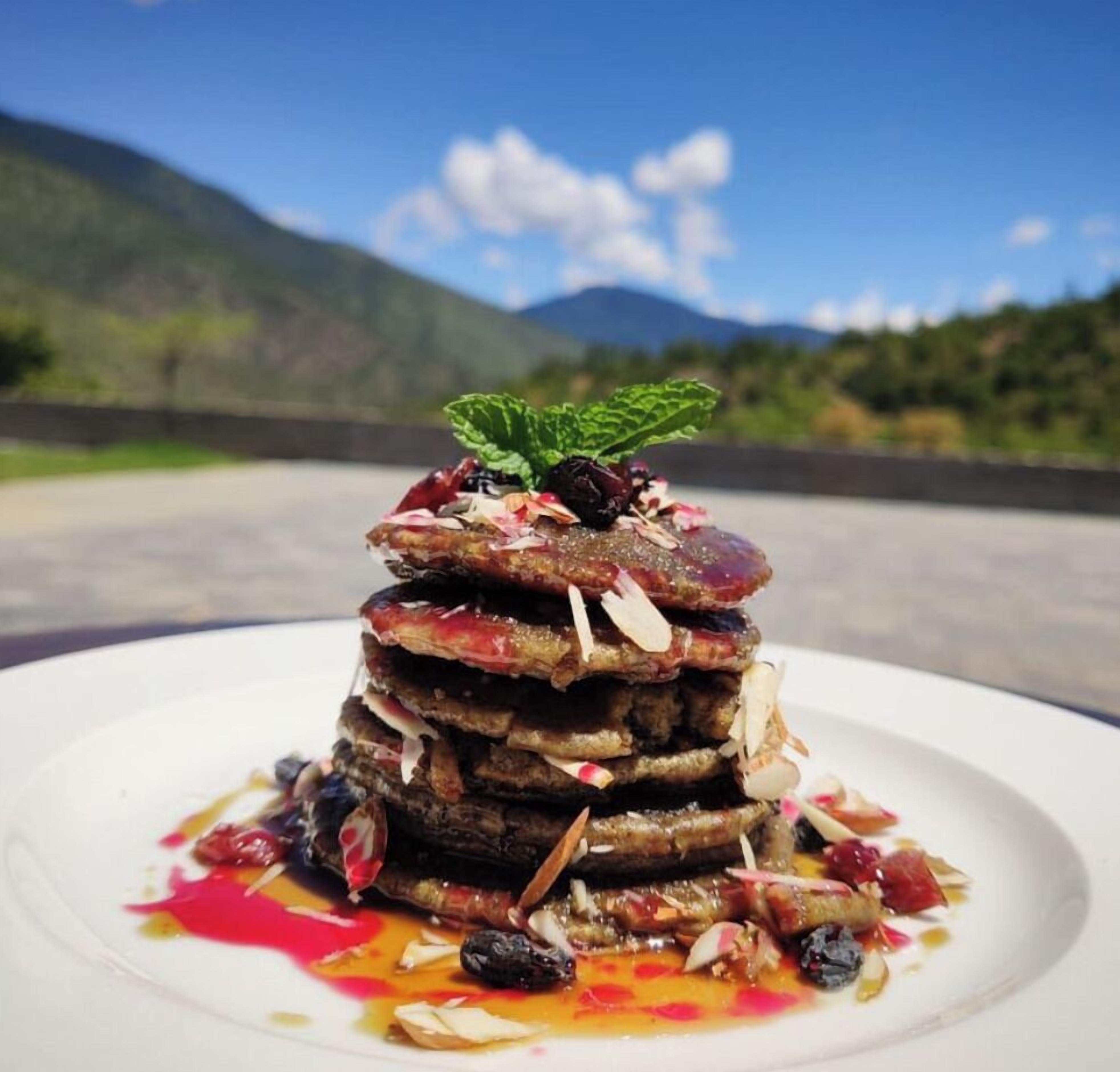 A stack of pancakes on a white plate with a scenic mountain view in the background.