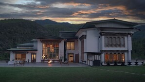 A modern house with large windows, a patio with outdoor furniture, and a view of the surrounding mountains. - The Postcard Dewa Thimphu (Thimphu)