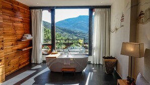 A bathroom with a large bathtub, a sink, and a window offering a mountain view. - The Postcard Dewa Thimphu (Thimphu)