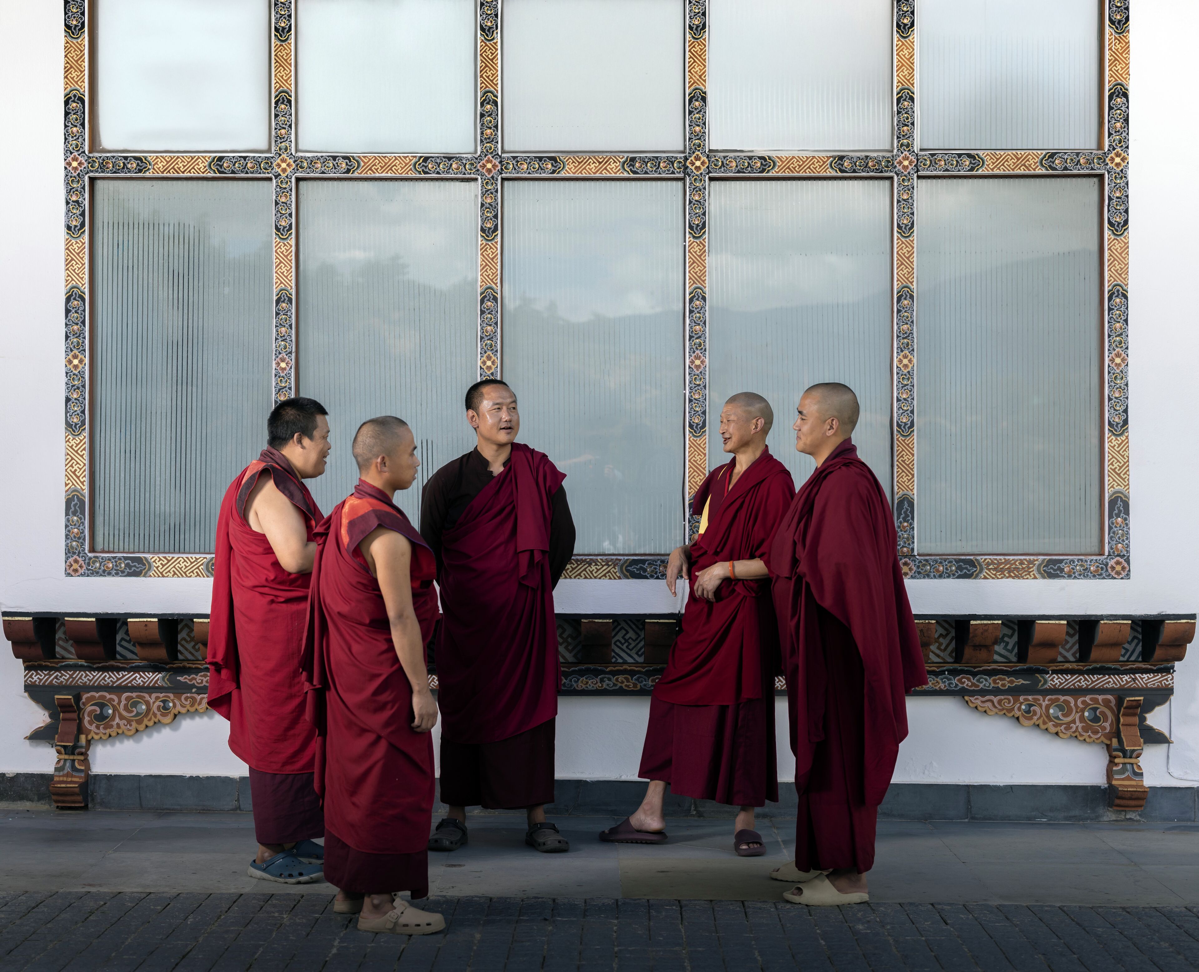 Monks in traditional robes standing in front of a building with large windows and decorative borders.