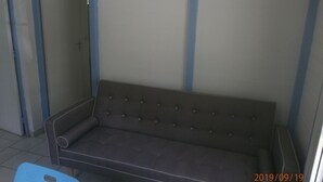 Een grijze bank met een bloemendecoratie aan de muur, een blauwe stoel en een deur op de achtergrond.