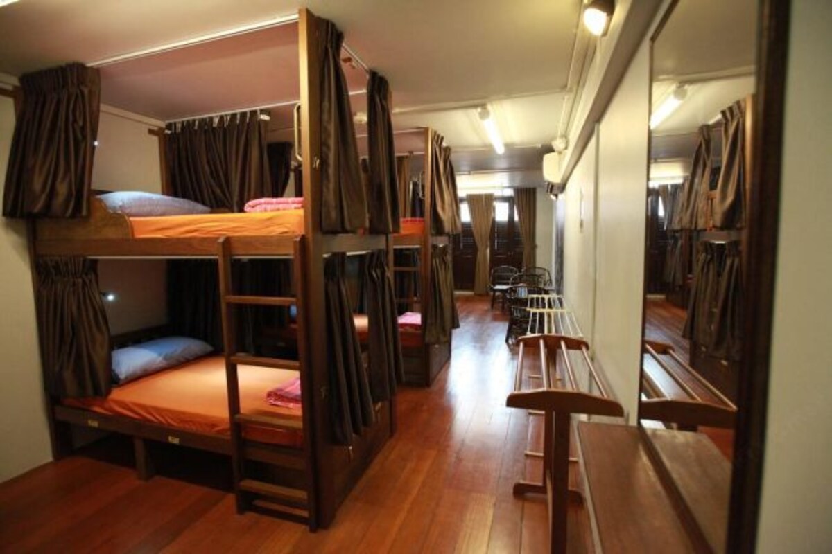 Dormitorio con literas, suelo de madera, un espejo y un banco.