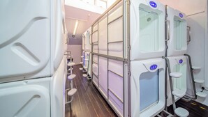 A row of white, modern, self-contained rooms with built-in amenities, including a small table and a chair, and a control panel on the wall. - K Space Inn 569 - Hostel (Singapore)