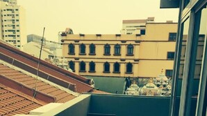 A balcony with a wooden bench and two small tables, overlooking a cityscape with buildings and a temple. - K Space Inn 569 - Hostel (Singapore)