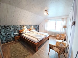 Une chambre à coucher avec un lit en bois, une chaise en osier et un radiateur.