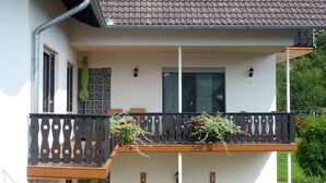 Una casa de dos pisos con un balcón, una ventana con cortina y un ventanalito en el piso superior.