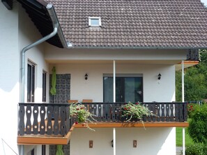 Une maison à deux étages avec un balcon, une fenêtre avec un rideau et une petite fenêtre à l’étage supérieur.