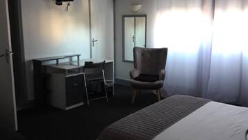 A hotel room with a bed, a desk with a chair, a television mounted on the wall, and a window with curtains.