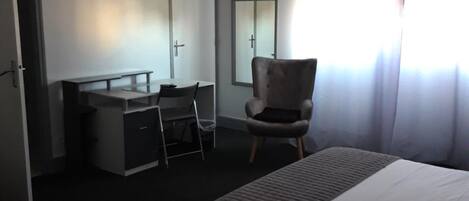 A hotel room with a bed, a desk with a chair, a television mounted on the wall, and a window with curtains.