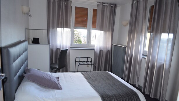 Een hotelkamer met een bed, bureau, stoel en raam met gordijnen.