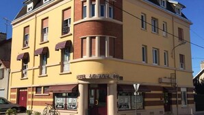 Een hotel met meerdere verdiepingen, een geel gevel, een rode deur en een bord waarop staat 