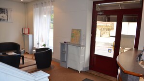 Een receptie met een rode deur, een witte radiator, een kaart op een plank en twee zwarte stoelen.