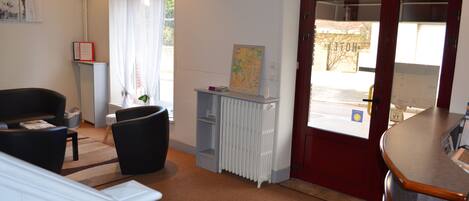 Un área de recepción con una puerta roja, un radiador blanco, un mapa en una estantería y dos sillas negras.