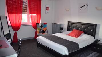 A bedroom with a bed, red curtains, a radiator, a desk, and a chair.