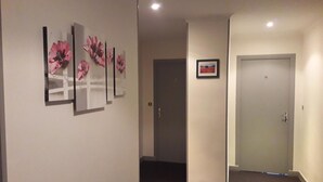 Een gang met een deur, een lijst met een afbeelding en drie verticale kunstwerken aan de muur.