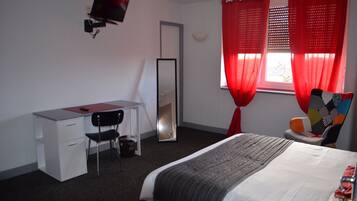 Een hotelkamer met een bed, een bureau, een stoel, een spiegel en rode gordijnen.