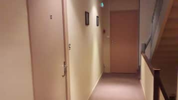 A hallway with carpeted floors, a wooden handrail, and a door on the left.