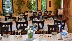 Un espace repas avec plusieurs tables dressées pour le service, chacune étant équipée de chaises, de couverts et de verres.