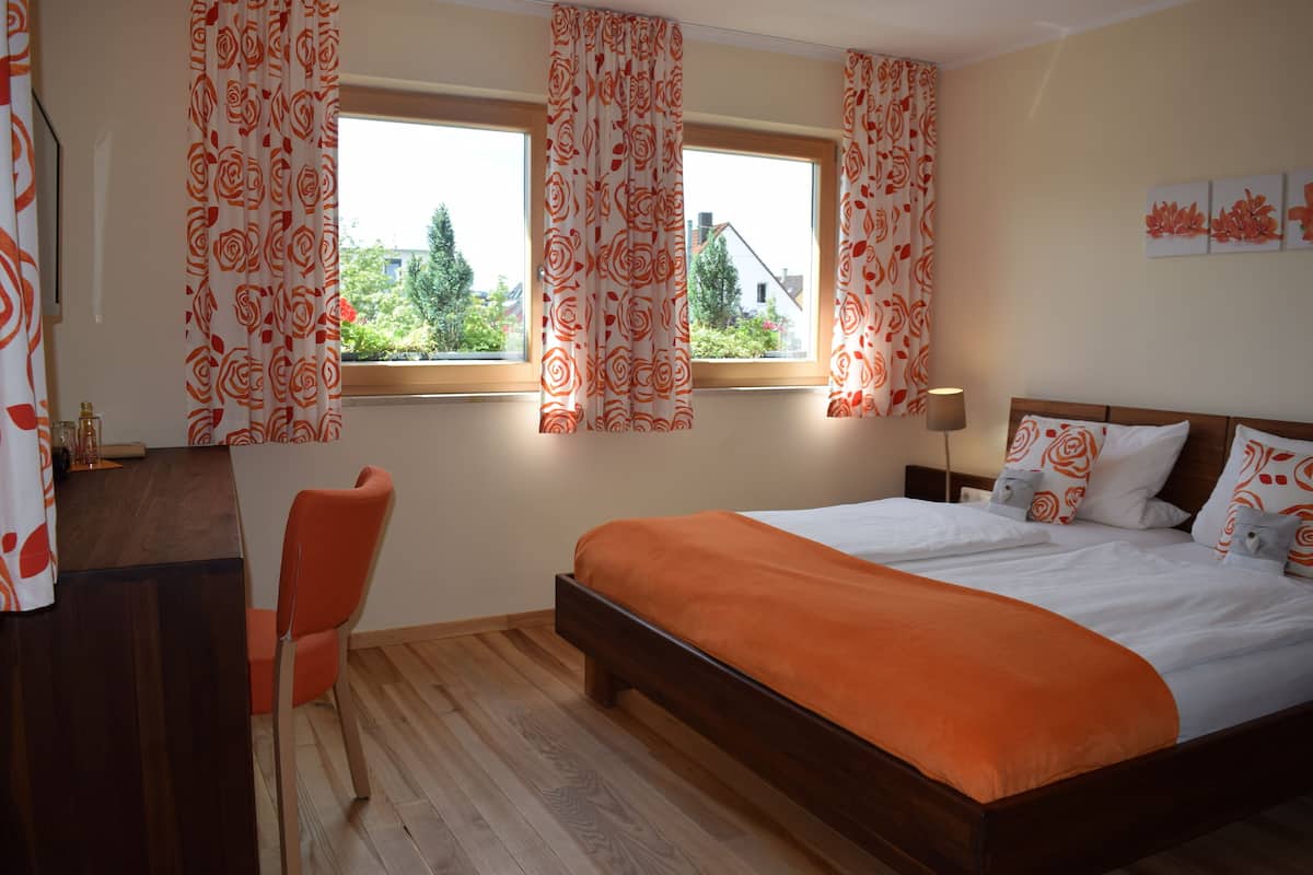 Une chambre à coucher avec un lit en bois, une literie orange, un bureau avec une chaise et une fenêtre avec des rideaux.