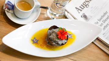 A dessert on a white plate with a yellow sauce, a cup of coffee, a glass of water, and a menu on a wooden table.