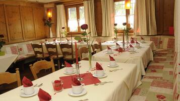 Un comedor con varias mesas dispuestas para el servicio, paneles de madera en las paredes y ventanas amplias con cortinas.