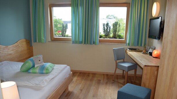 Ein Zimmer mit einem Bett, einem Schreibtisch, einem Stuhl, einem Fernseher und einem Vorhangfenster.