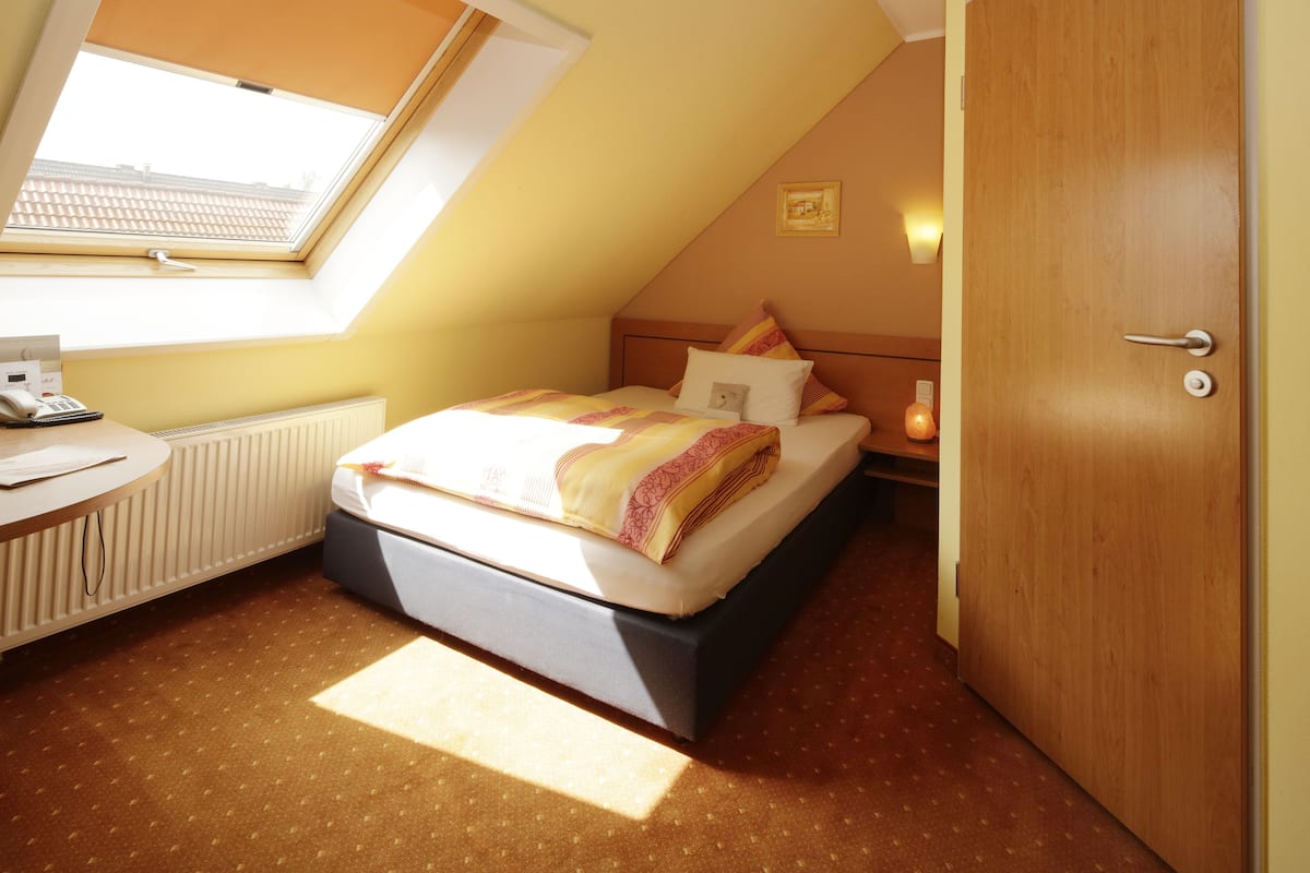 Une chambre à coucher avec un lit, un bureau, un radiateur, une porte en bois et un puits de lumière.