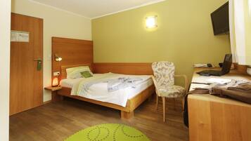 Ein Hotelzimmer mit einem hölzernen Bett, einem Schreibtisch mit Stuhl, einem grünen Teppich und einem an der Wand befestigten Fernseher.