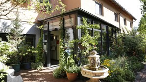 Un hôtel avec une entrée en verre, des plantes en pot et une fontaine.