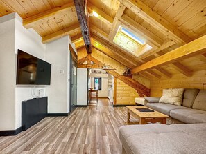 Un loft espacioso con techo alto, vigas de madera, un televisor montado en la pared, un sofá y una escalera que lleva a un nivel superior.