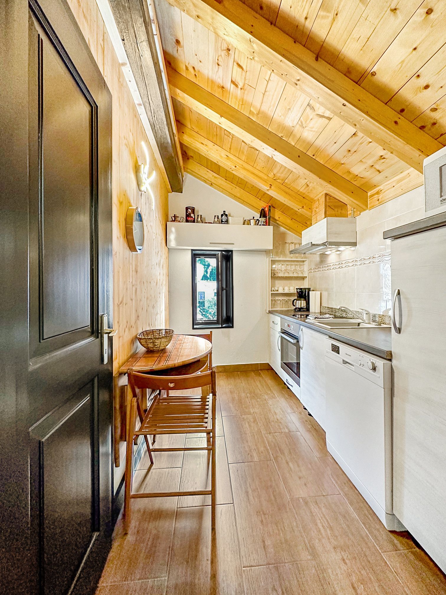 Una cocina con vigas de madera, una mesa de comedor con sillas, un refrigerador y un ventanal con vistas.