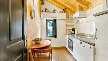 Una cocina con vigas de madera, una mesa de comedor con sillas, un refrigerador y un ventanal con vistas.