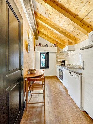 A kitchen with wooden beams, a dining table with chairs, a refrigerator, and a window with a view. - Cosy & Star - Salvan - Les Marécottes - Swiss Alps (Salvan)