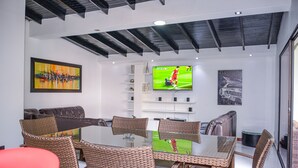 A modern living room with a glass-top dining table, wicker chairs, a leather sofa, and a flat-screen TV mounted on the wall. - 6 Bedroom 7 bath AC, Hot tub Balcony Poblado. No guest fees no register guests. (Medellín)
