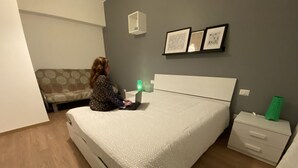 A bedroom with a bed, a nightstand, a lamp, a couch, and framed pictures on the wall. - Holiday Home - Home Holiday - Cozy House Matera - Blue House - VERY CENTRAL (Matera)