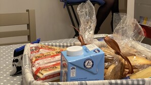 A person working at a desk in a room with a bed, a chair, and various items on the bed including a box of milk, a bag of Doritos, and a loaf of bread. - Holiday Home - Home Holiday - Cozy House Matera - Blue House - VERY CENTRAL (Matera)