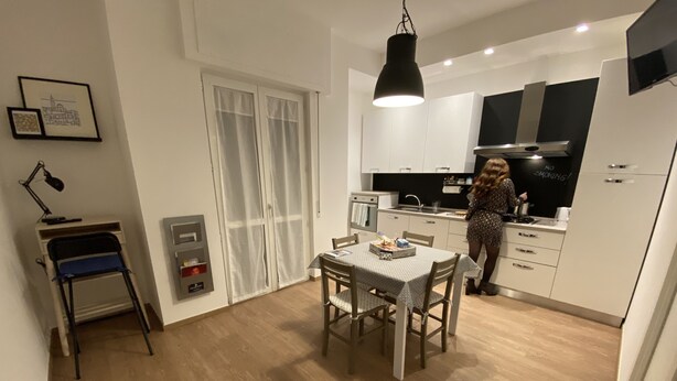 A modern kitchen with white cabinets, a black range hood, and a person cooking. - Holiday Home - Home Holiday - Cozy House Matera - Blue House - VERY CENTRAL (Matera)