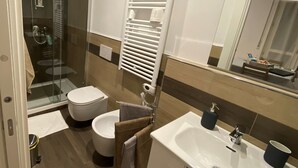 A modern bathroom with a glass shower enclosure, a toilet, a sink with a mirror, and a towel rack. - Holiday Home - Home Holiday - Cozy House Matera - Blue House - VERY CENTRAL (Matera)