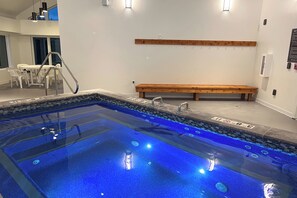 Ein Pool mit einer Holzbank, einem Tisch mit Stühlen und einer Treppe, die zum Pool führt.