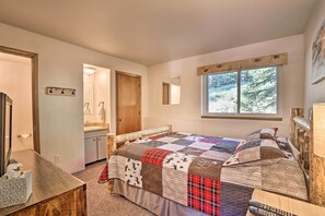 Ein Schlafzimmer mit einem großen Bett, einem Holzkopfteil, einem Nachttisch, einem Schreibtisch und einem Fenster mit Blick auf Bäume.