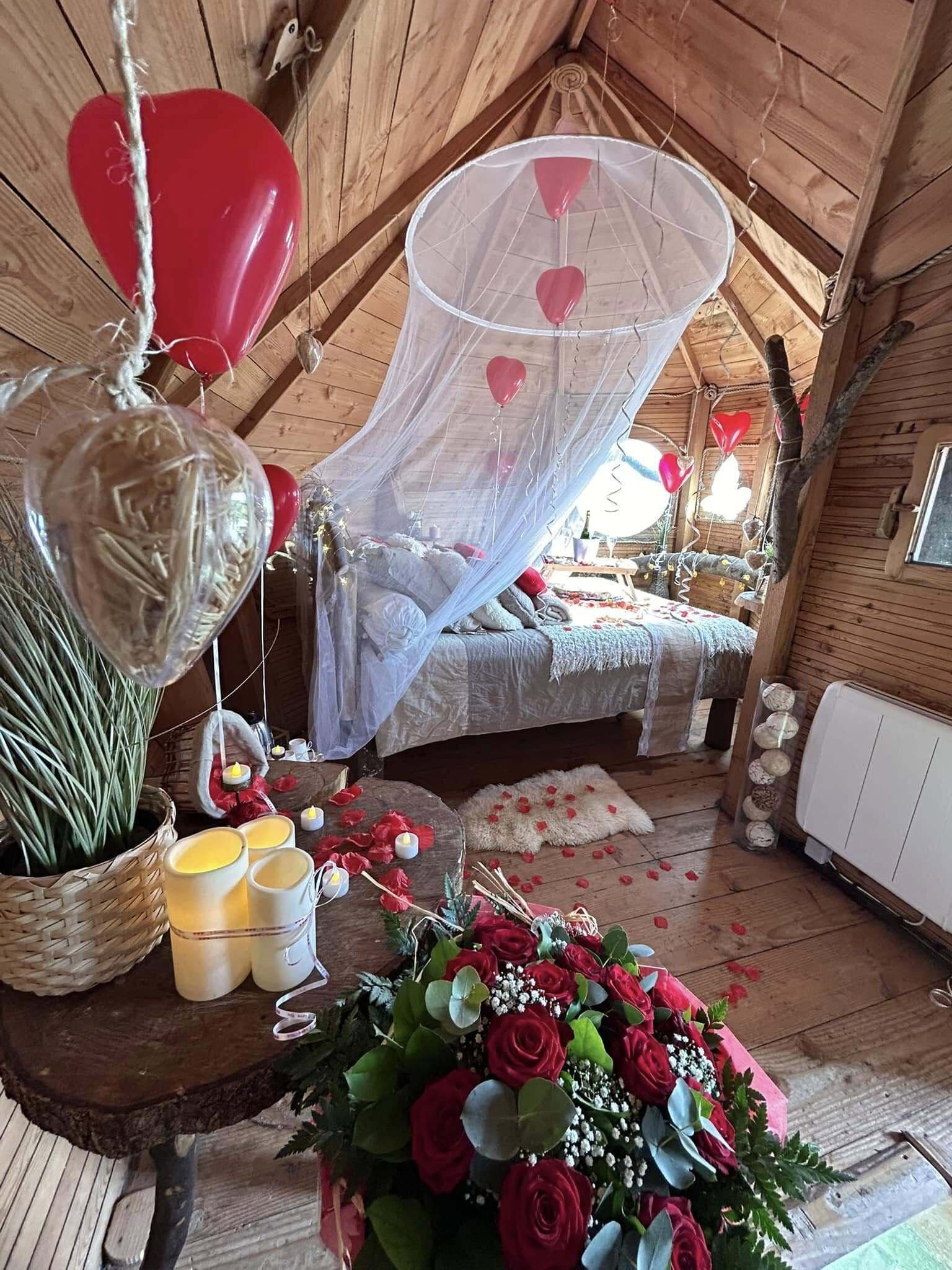Une chambre à coucher chaleureuse et rustique, dotée d’un lit à baldaquin, d’un plancher en bois et d’une composition décorative de fleurs et de bougies.