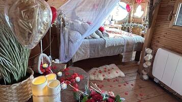 Une chambre à coucher chaleureuse et rustique, dotée d’un lit à baldaquin, d’un plancher en bois et d’une composition décorative de fleurs et de bougies.