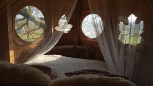 A cozy room with a bed, a wooden headboard, and a large window with a view of trees. - Le Domaine de Wail Legends Resort (Wail)