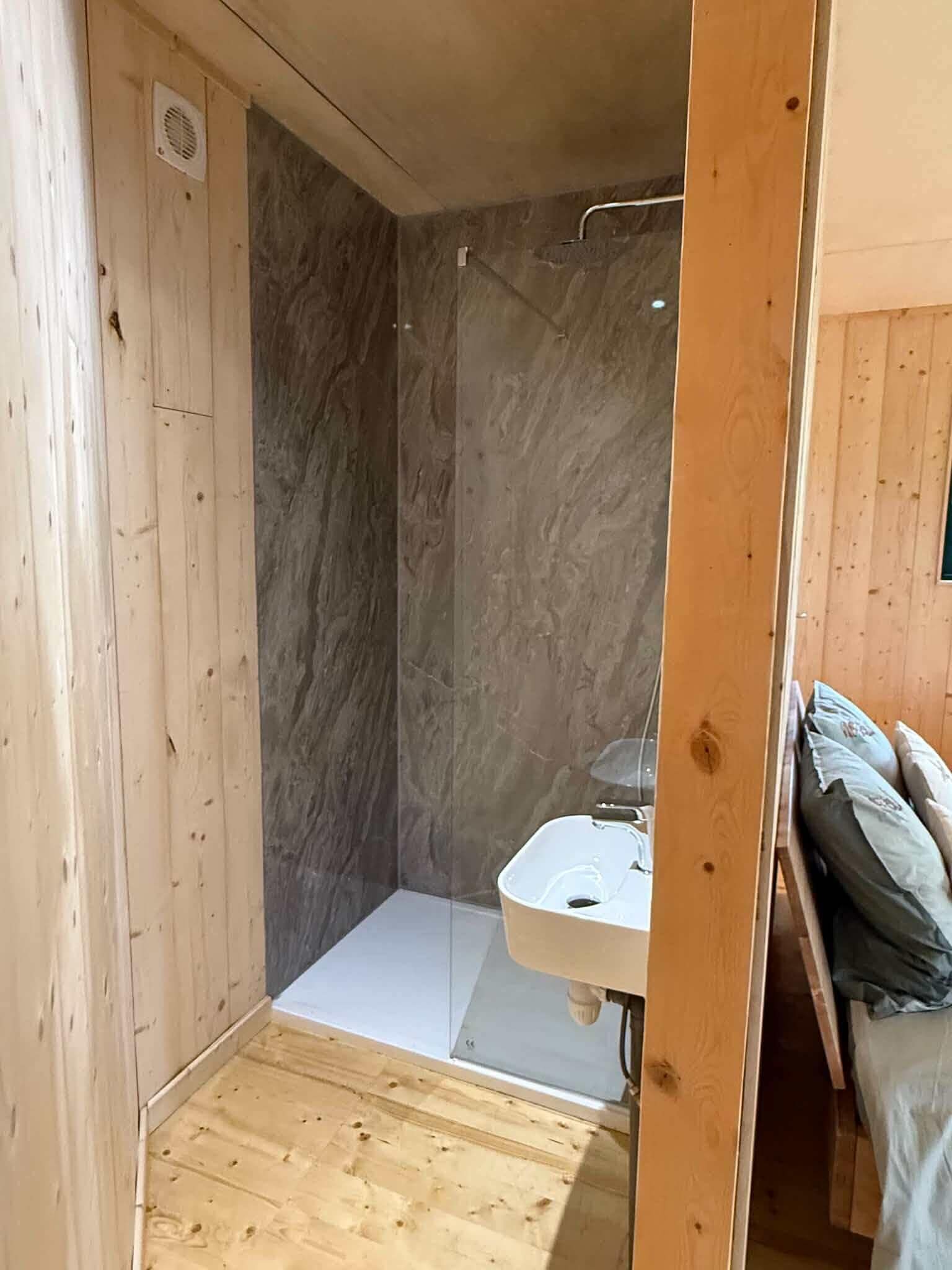 A small, enclosed shower area with a white sink and wooden walls.